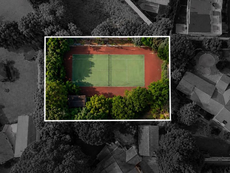Aerial view of a private tennis court surrounded by mature trees and residential landscaping.