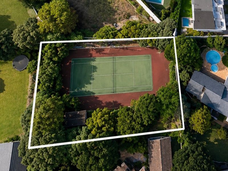 Aerial view of a private residential tennis court surrounded by mature trees and perimeter fencing.