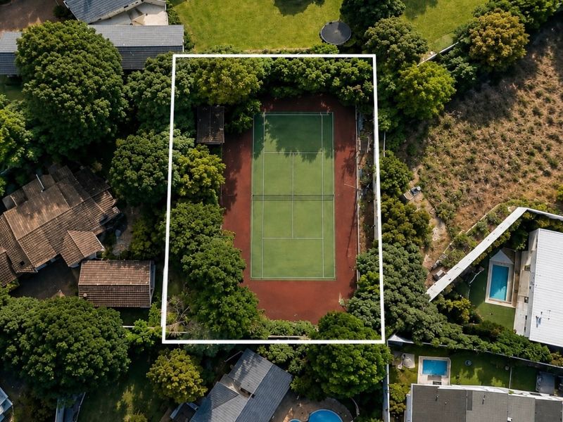 Aerial view of a residential property featuring a private tennis court surrounded by mature trees and established landscaping.