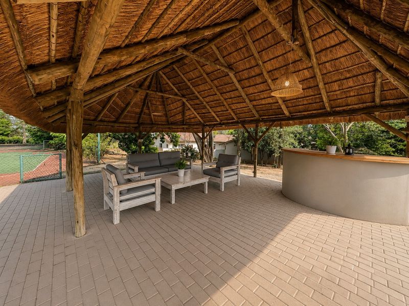A spacious covered outdoor patio featuring a traditional thatched roof, timber support structure, paved flooring, and a built-in bar counter.