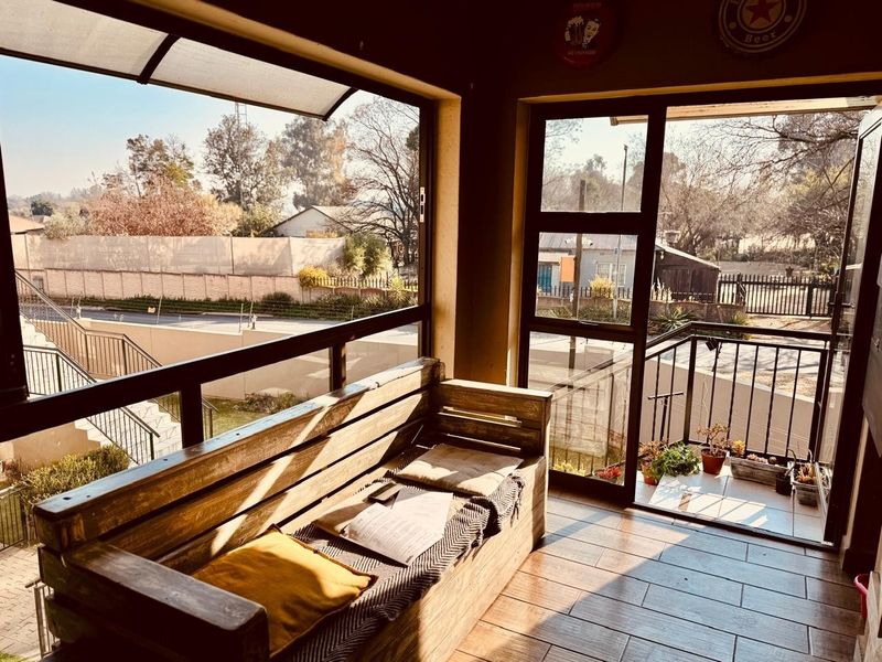 A bright, enclosed balcony featuring tiled flooring, large windows providing ample natural light, and metal safety railings overlooking the surrounding area.