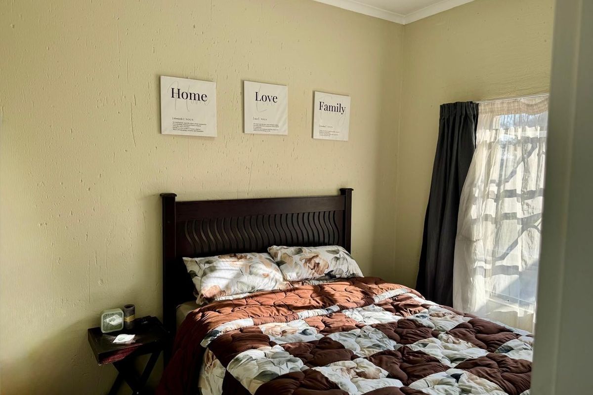 A standard bedroom featuring textured walls and a window with installed curtain rails, providing natural light.