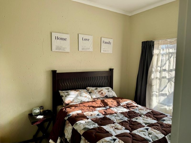 A standard bedroom featuring textured walls and a window with installed curtain rails, providing natural light.