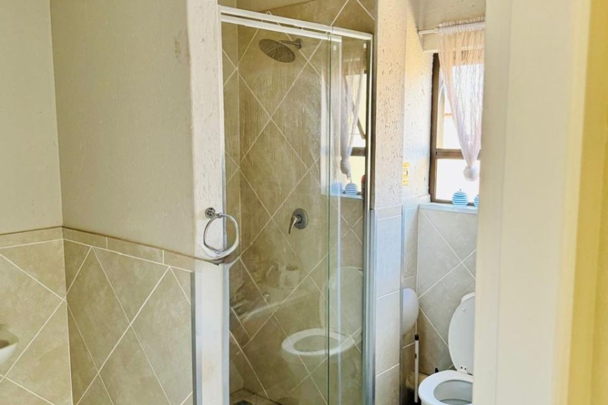 A functional bathroom featuring a glass-enclosed shower, toilet, and neutral tiled finishes throughout.