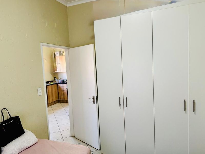 Bedroom featuring a large white built-in wardrobe and tiled flooring, with a view through the doorway into the adjacent kitchen area.