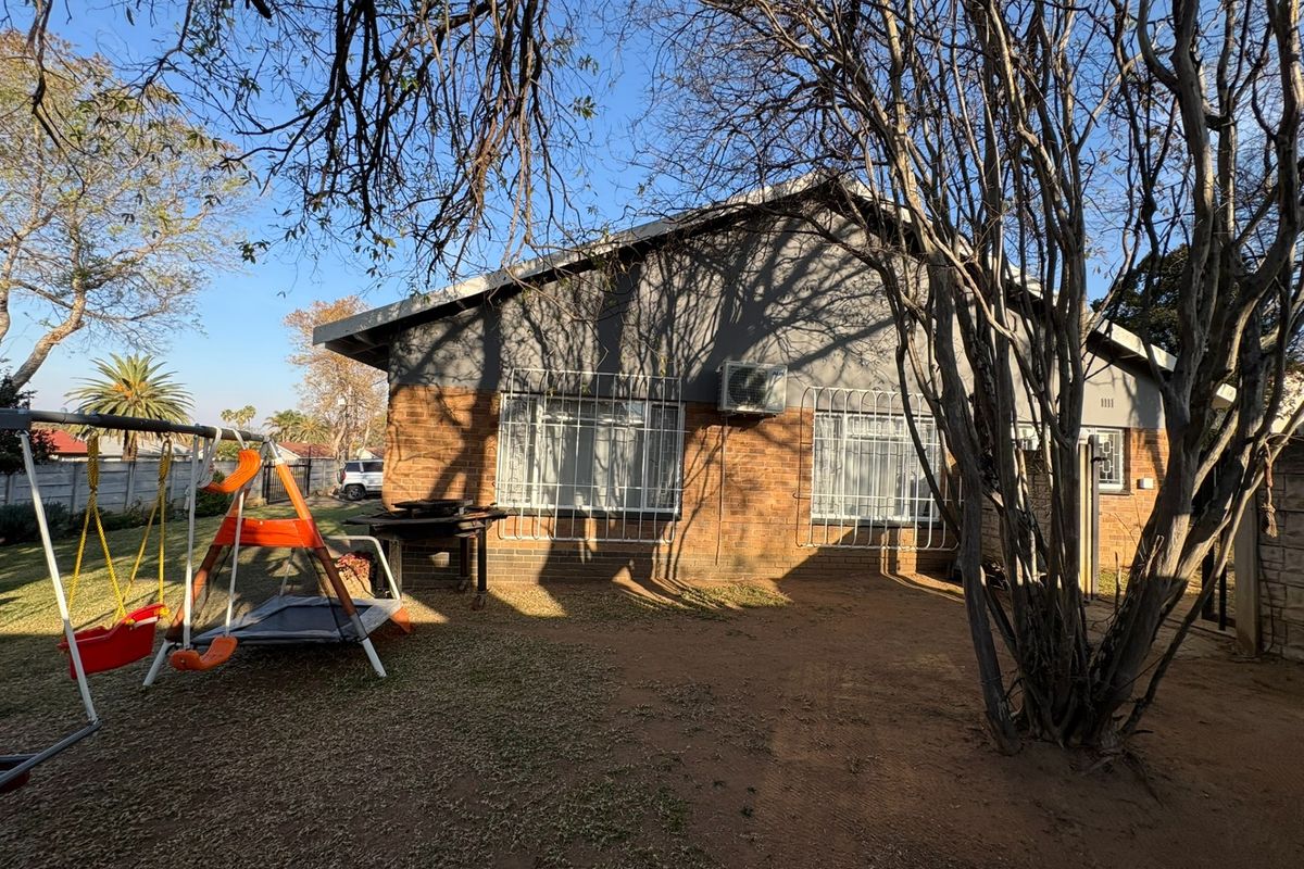 Rear view of the house featuring a brick facade, security bars on windows, and an installed air conditioning unit set within a garden area.