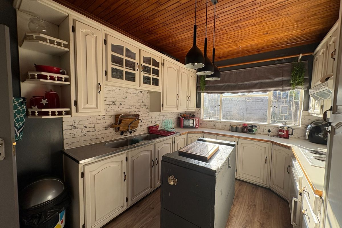 A functional kitchen featuring classic cabinetry, a double sink, timber-paneled ceiling, and pendant lighting, offering a warm and traditional aesthetic.