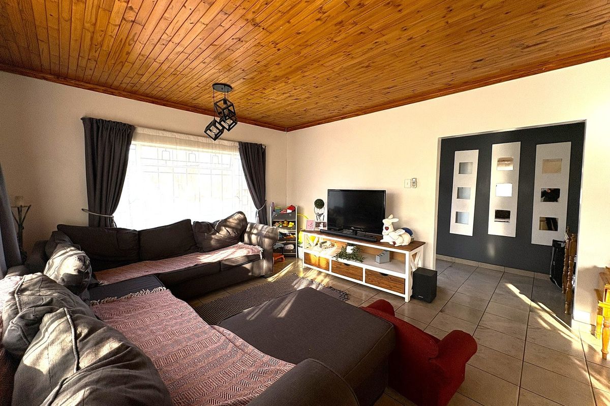 A living room featuring a warm timber tongue and groove ceiling, ceramic floor tiles, and natural light through a window with security bars.