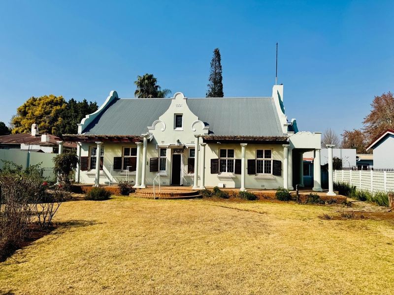 A charming historic-style house featuring a gabled facade, corrugated metal roof, and a spacious front veranda supported by classical columns.