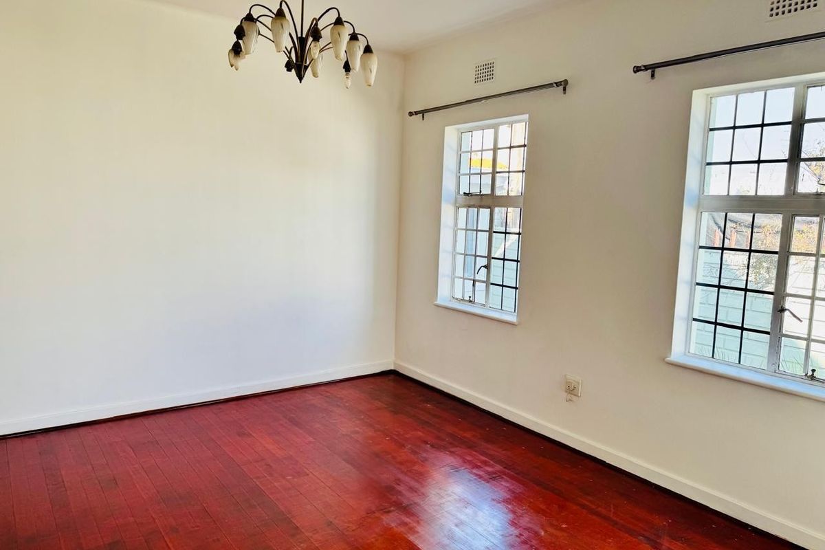 A bright, empty bedroom featuring polished hardwood flooring, leaded glass windows, and a classic ceiling light fixture.