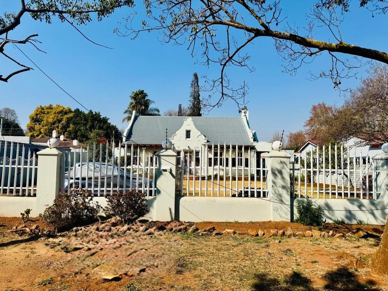 Front view of a traditional house featuring a gabled roof, secured by a metal perimeter fence with masonry pillars.