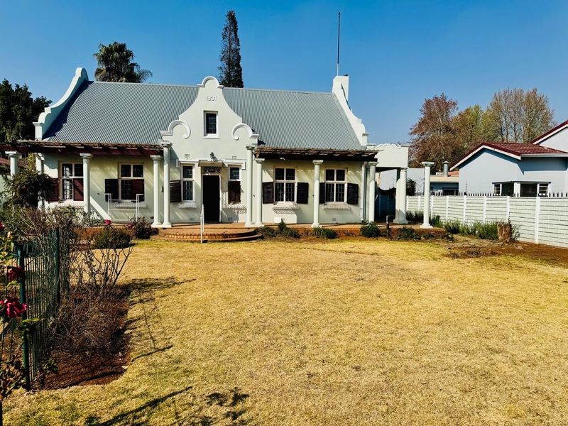 A charming historic Cape Dutch style home featuring a gabled facade, corrugated metal roof, and a welcoming front veranda with classical columns.