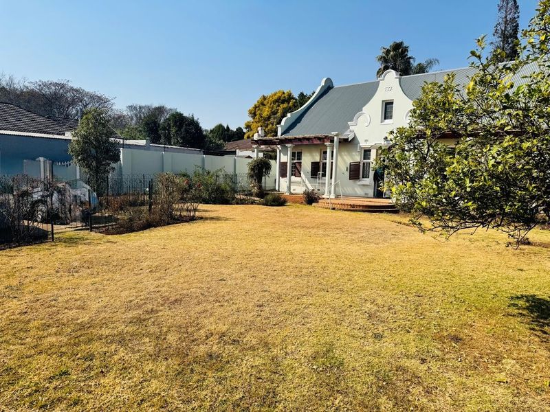 A view of the rear garden and the back elevation of a historic-style house featuring a gabled roof and a covered patio area.