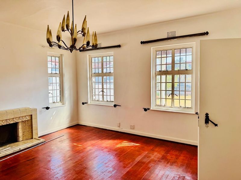 A bright, empty living room featuring original hardwood flooring, a classic tiled fireplace, and charming leaded glass windows.