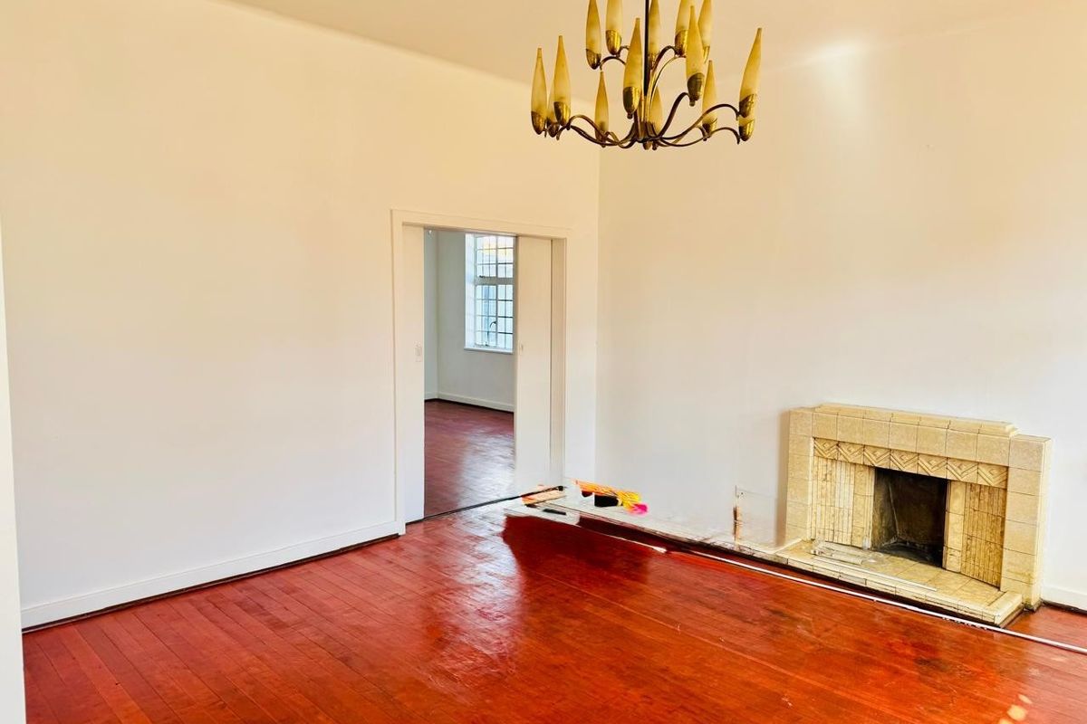 An empty living room featuring polished hardwood floors, a vintage tiled fireplace, and a classic chandelier, offering a blank canvas for interior design.