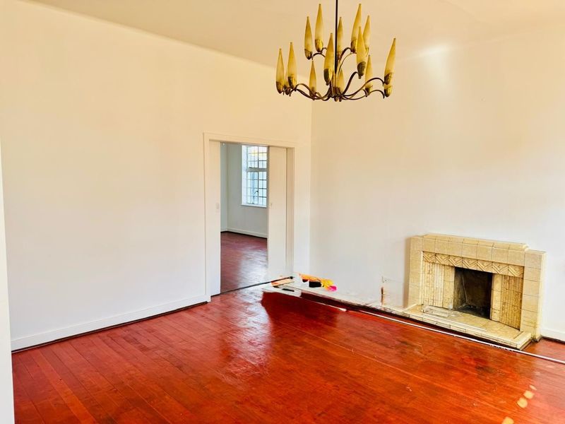 An empty living room featuring polished hardwood floors, a vintage tiled fireplace, and a classic chandelier, offering a blank canvas for interior design.