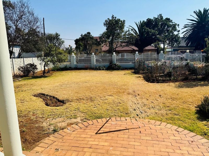 A spacious backyard featuring a brick-paved patio area, established lawn, and secure perimeter wall with metal fencing.
