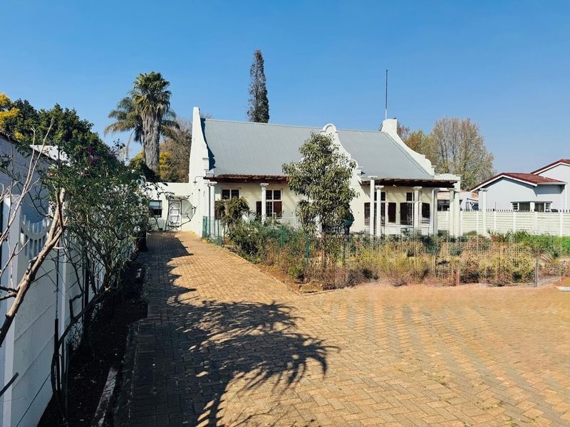 A view of the rear elevation of a house featuring a gabled corrugated metal roof, a paved driveway, and a covered patio area.