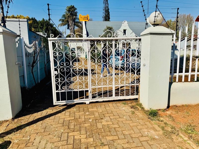 Front entrance featuring a white wrought iron gate, paved driveway, and perimeter electric fencing.