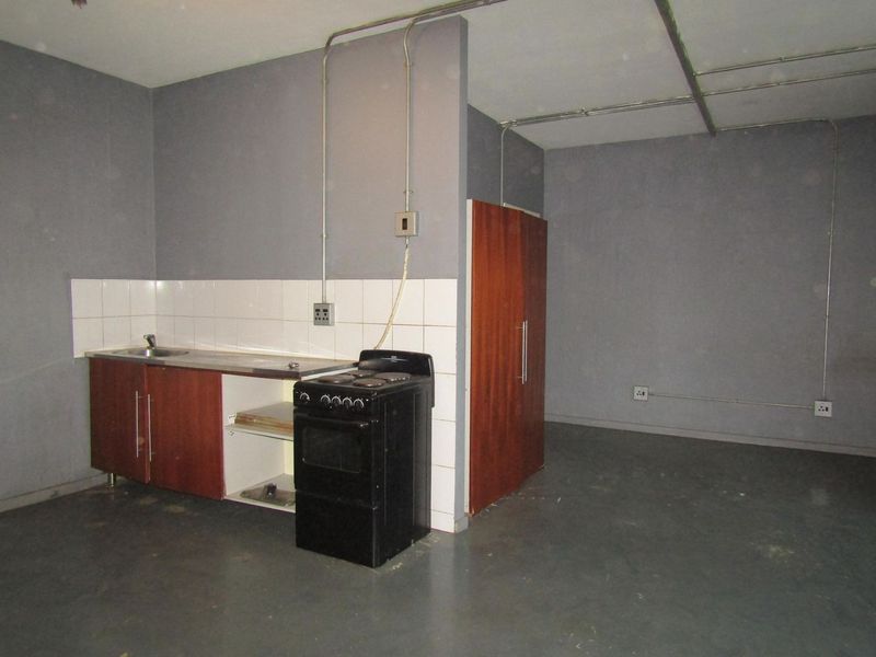 A basic, empty kitchen area featuring a small kitchenette with a sink, tiled backsplash, and a freestanding stove, requiring cosmetic updates.