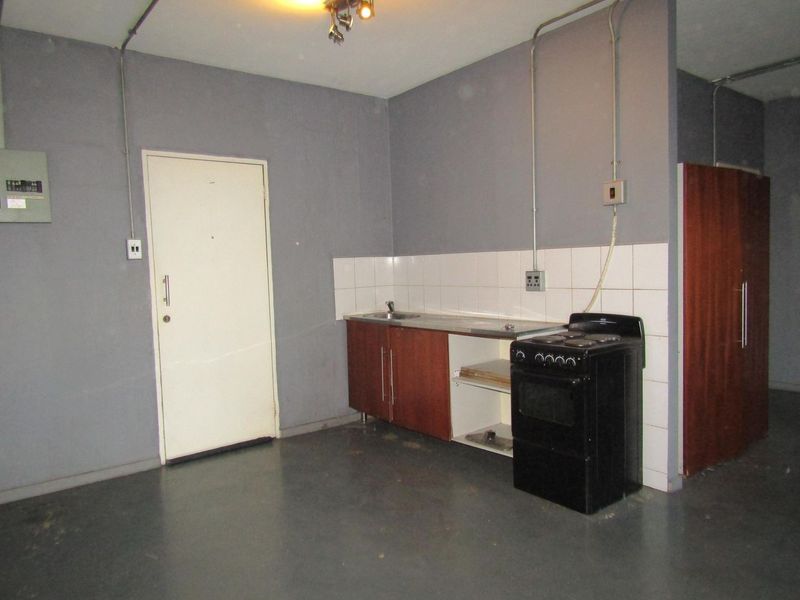 A basic, functional kitchen area featuring simple cabinetry, a stainless steel sink, tiled splashback, and a freestanding stove with exposed electrical conduit.