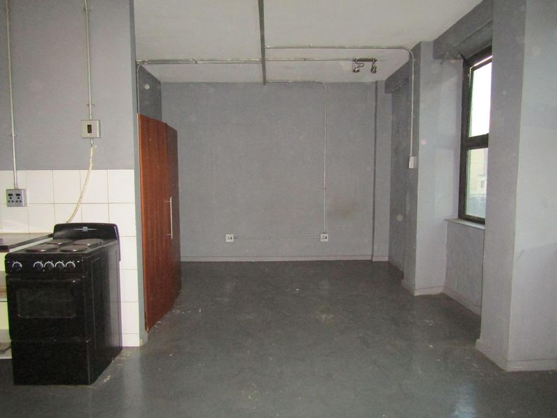 An empty kitchen area featuring exposed electrical conduit, a freestanding stove, and basic tiled splashback, requiring significant cosmetic updates and finishing.