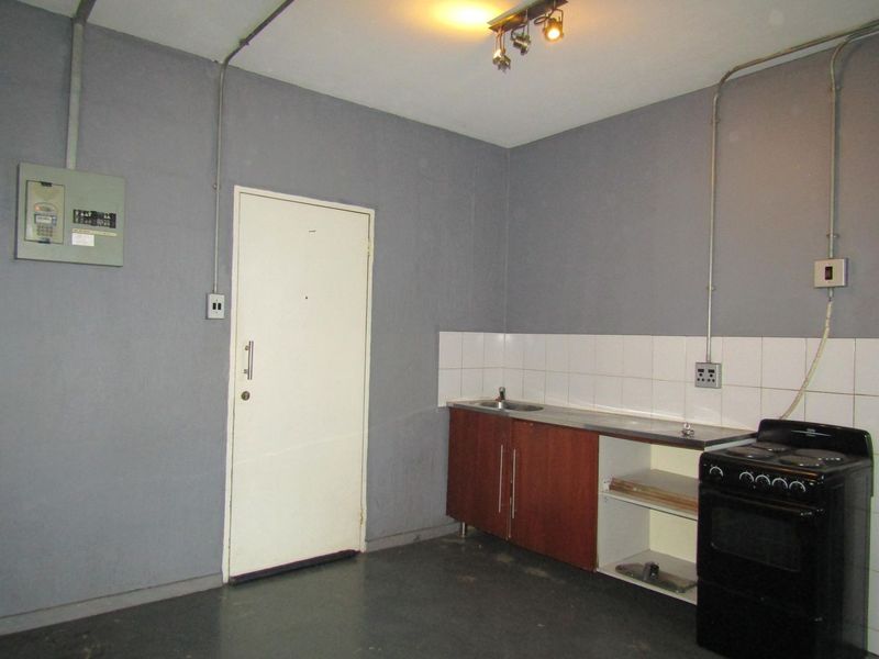 A functional kitchen area featuring basic cabinetry, a stainless steel sink, tiled splashback, and a freestanding stove, with exposed electrical conduit.