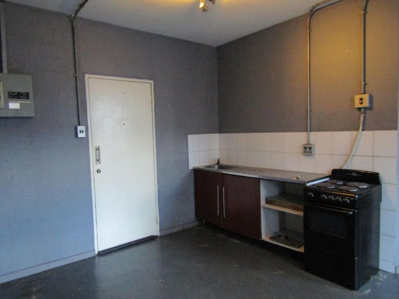 A basic, functional kitchen area featuring a stainless steel sink, tiled splashback, and a freestanding stove with exposed electrical infrastructure.