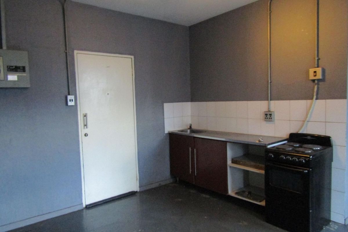 A basic, functional kitchen area featuring a stainless steel sink, tiled splashback, and a freestanding stove with exposed electrical infrastructure.