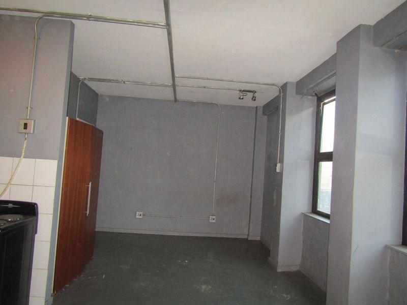 An empty open-plan living area featuring exposed electrical conduit, grey painted walls, and a built-in cupboard, offering a blank canvas for renovation.