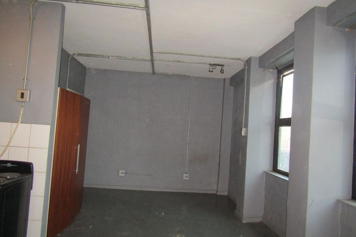 An empty open-plan living area featuring exposed electrical conduit, grey painted walls, and a built-in cupboard, offering a blank canvas for renovation.