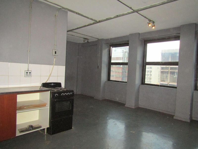 Open-plan living and kitchen area featuring industrial-style exposed conduit, concrete flooring, and large windows with urban views.