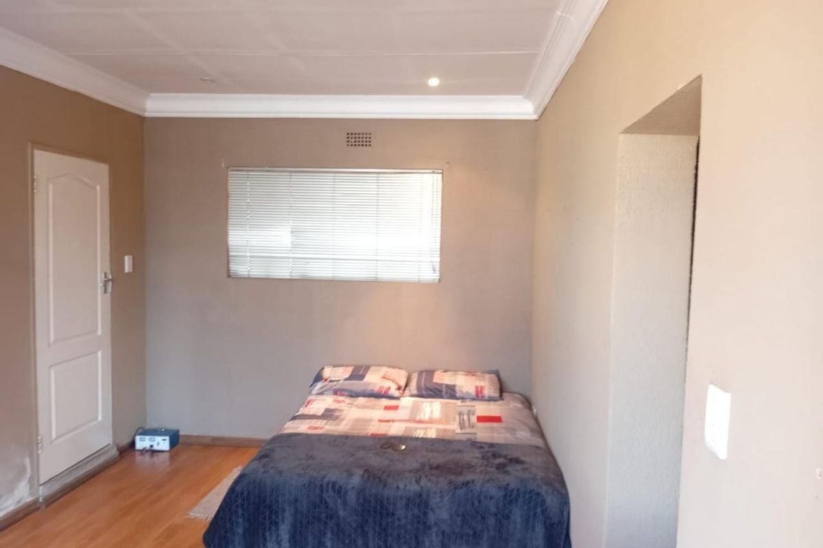 A functional bedroom featuring laminate flooring, neutral wall tones, and a window fitted with venetian blinds.