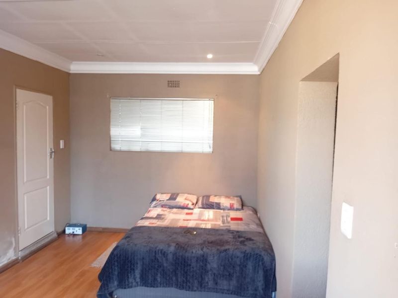 A functional bedroom featuring laminate flooring, neutral wall tones, and a window fitted with venetian blinds.