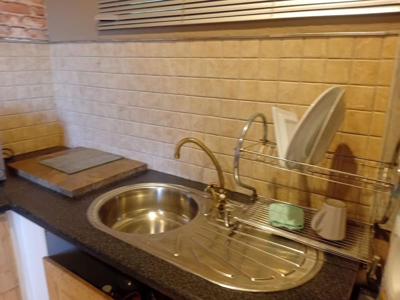 A functional kitchen area featuring a stainless steel sink with a brass faucet, tiled backsplash, and laminate countertops.