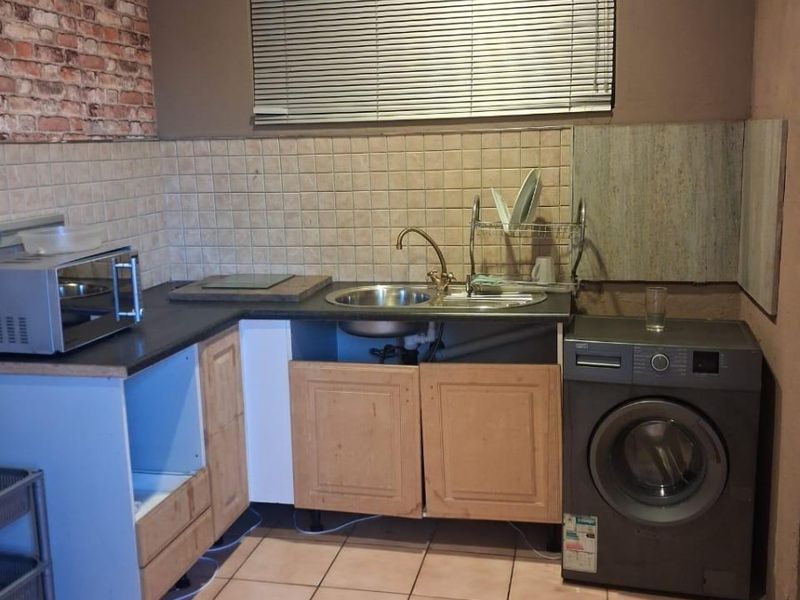 A functional kitchen area featuring tiled flooring, a stainless steel sink, and built-in cabinetry with some missing doors and visible wear.