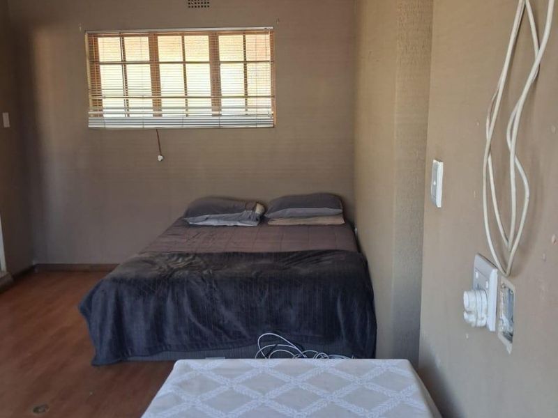 A bedroom featuring laminate flooring and a window with blinds, currently requiring attention to exposed electrical wiring and wall finishes.