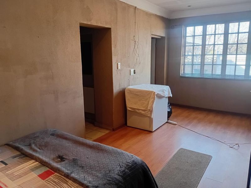 A bedroom featuring laminate flooring and a grid-pattern window, currently requiring wall finishing and electrical repairs to improve the overall aesthetic and functionality.