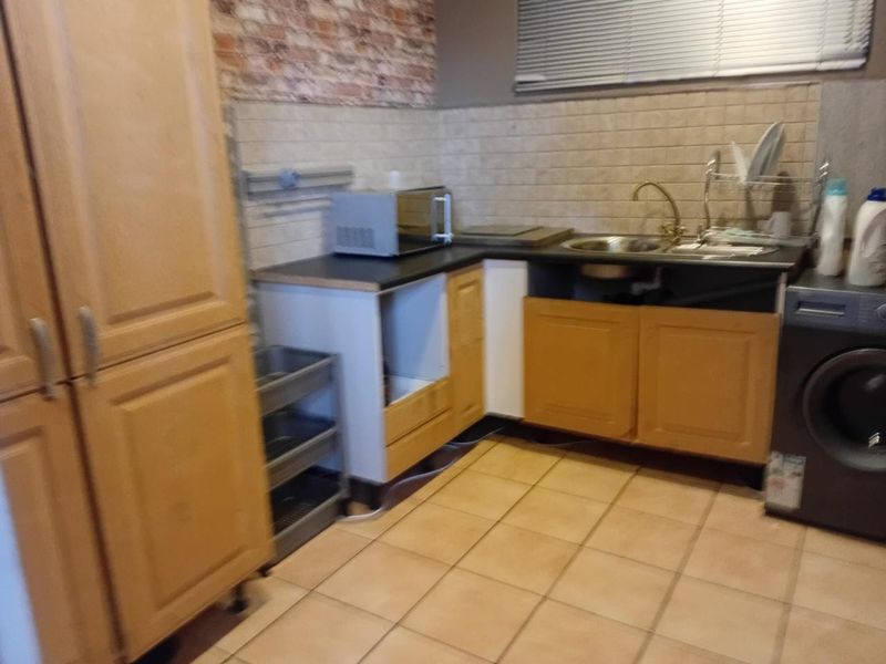 A functional kitchen area featuring wooden cabinetry, tiled backsplash, and ceramic flooring, currently showing signs of wear and missing cabinet components.