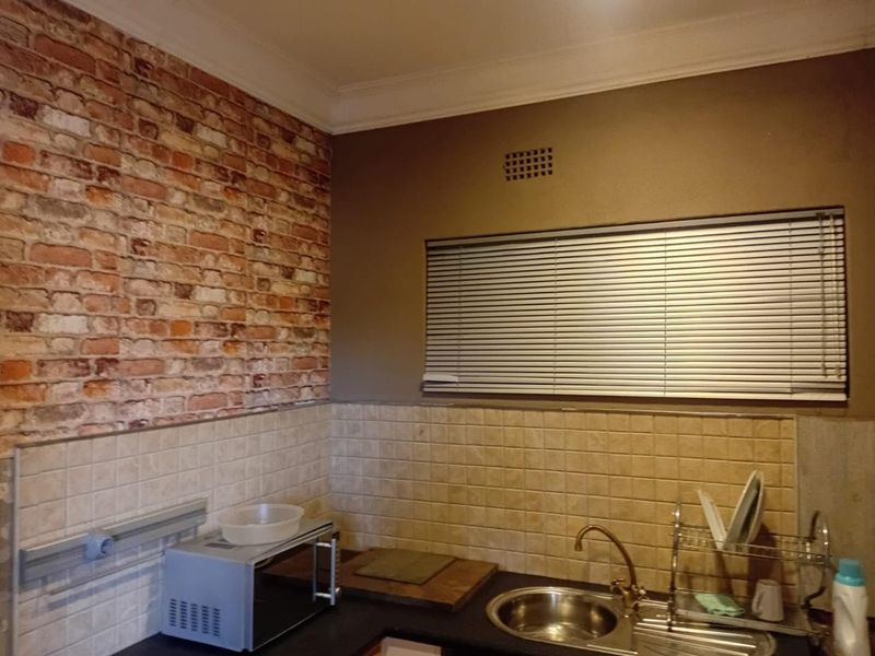 A functional kitchen area featuring a stainless steel sink, tiled splashback, and decorative brick-effect wall finish with venetian blinds.
