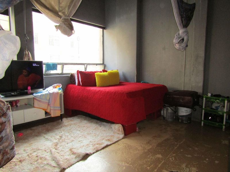 A bedroom featuring a large window and unfinished concrete flooring, offering a blank canvas for renovation and interior design updates.