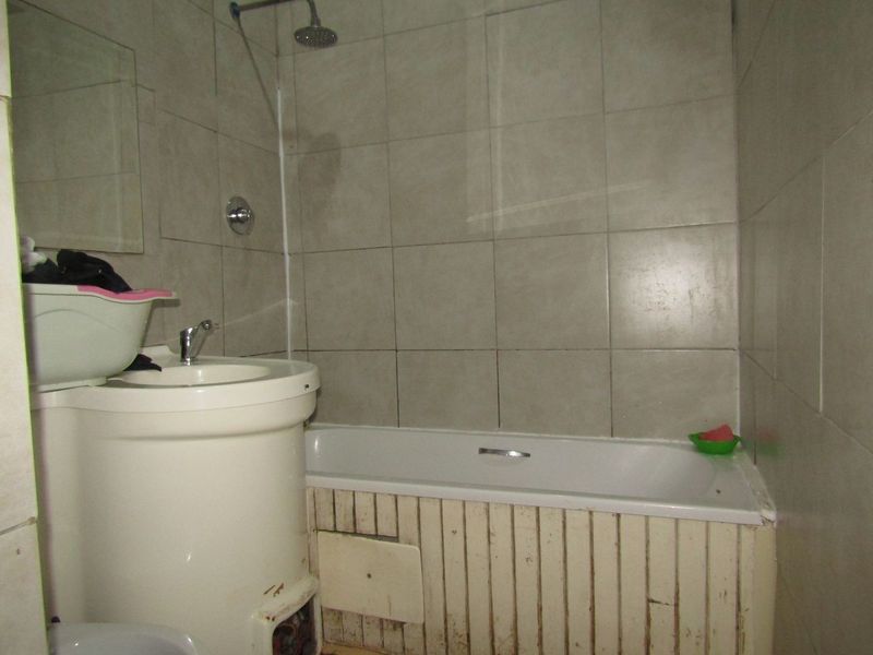 A functional bathroom featuring a bathtub with shower head, pedestal basin, and tiled walls. The space shows signs of wear and requires cosmetic updates.