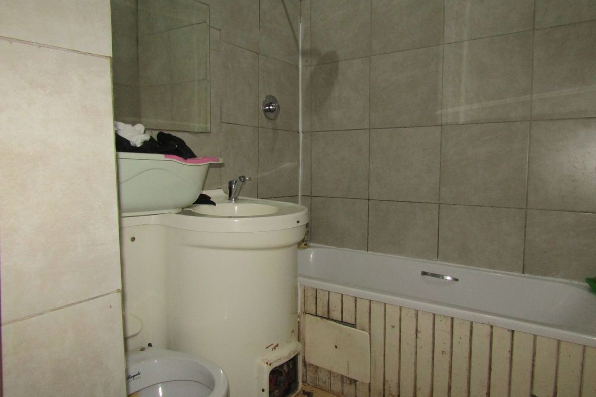 A dated bathroom featuring a bathtub with shower head, pedestal basin, and toilet, requiring significant refurbishment of finishes and fixtures.