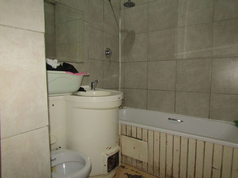 A dated bathroom featuring a bathtub with shower head, pedestal basin, and toilet, requiring significant refurbishment of finishes and fixtures.