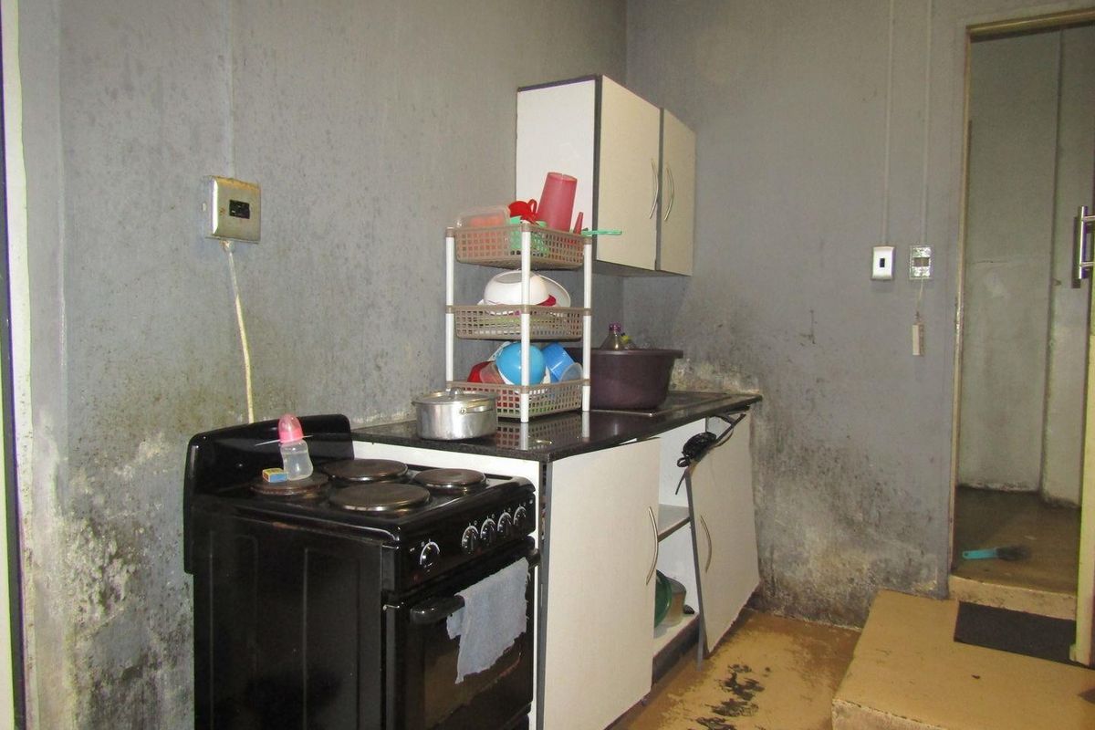 A small kitchen area featuring basic cabinetry and an electric stove, currently requiring significant maintenance and cosmetic renovation to improve the wall and floor finishes.
