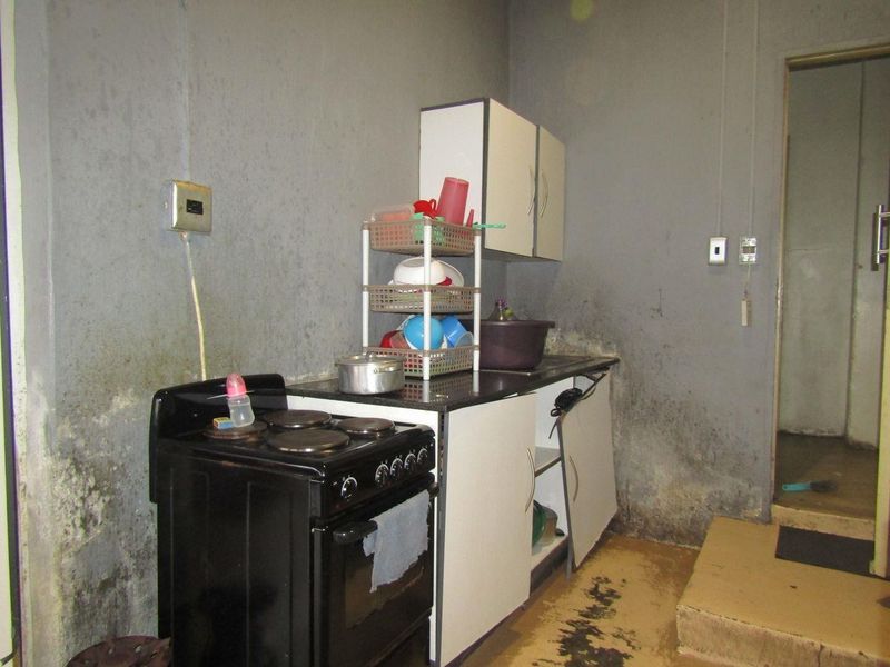A small kitchen area featuring basic cabinetry and an electric stove, currently requiring significant maintenance and cosmetic renovation to improve the wall and floor finishes.