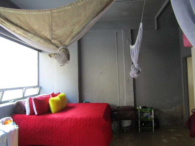 A bedroom featuring large windows and exposed concrete walls, requiring cosmetic updates and finishing to improve the overall aesthetic and condition.