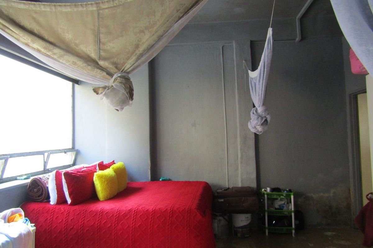 A bedroom featuring large windows and exposed concrete walls, requiring cosmetic updates and finishing to improve the overall aesthetic and condition.