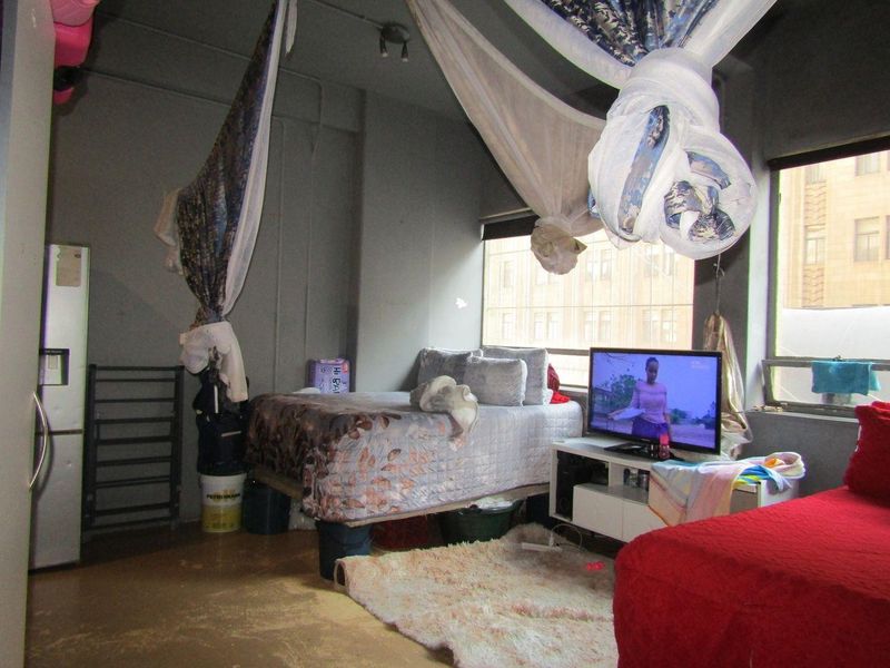 A bedroom featuring industrial-style exposed concrete ceilings and walls with large windows, requiring cosmetic updates to improve the overall finish and appeal.