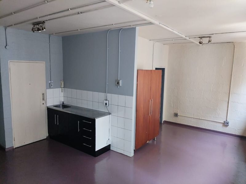 A compact, empty kitchen area featuring basic cabinetry, a sink, and exposed electrical conduit, offering potential for modernization and renovation.
